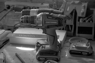 Close-up of a sleek cordless power drill resting on a wooden workbench with scattered screws.