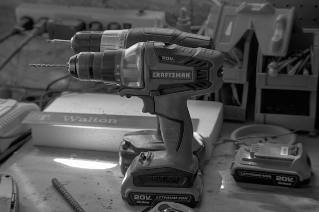 A close-up of a modern cordless drill resting on a wooden workbench with tools in the background