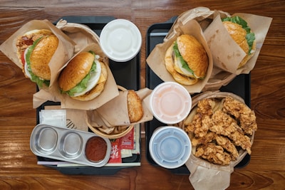 Overhead view of a colorful fast food platter with burgers, fries, and fresh salads on a red and gold tablecloth.