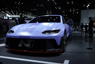 A sleek retro car glowing under neon pink and blue showroom lights.