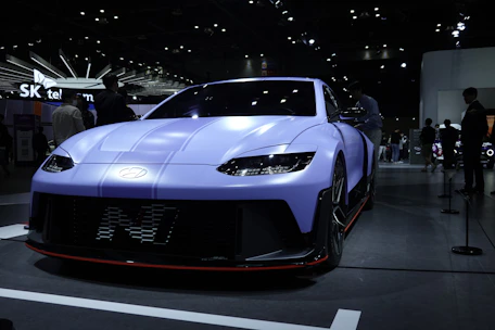 A sleek retro car glowing under neon pink and blue showroom lights.
