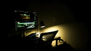 Dark-themed workspace with dual monitors showing complex video editing software and a cozy ambient light.