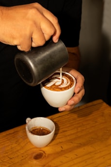 A close-up of a barista expertly pouring creamy milk into a freshly brewed cup of coffee at Aphrodite Coffee.