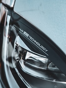 A close-up view of a car's headlight featuring 'JAGUAR LED TECHNOLOGY' branding. The image highlights the sleek and modern design of the headlight, showcasing materials like glass and metal.