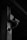 A surveillance camera is mounted on a metal pole, extending from a bracket. The setting appears to be industrial or urban, with shadows creating a dark, moody atmosphere.