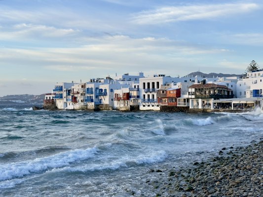 A row of houses sitting on top of a beach next to the ocean — Mykonos, Greece