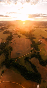 Wide view of a countryside property with a small lake, barn, and open fields at sunset