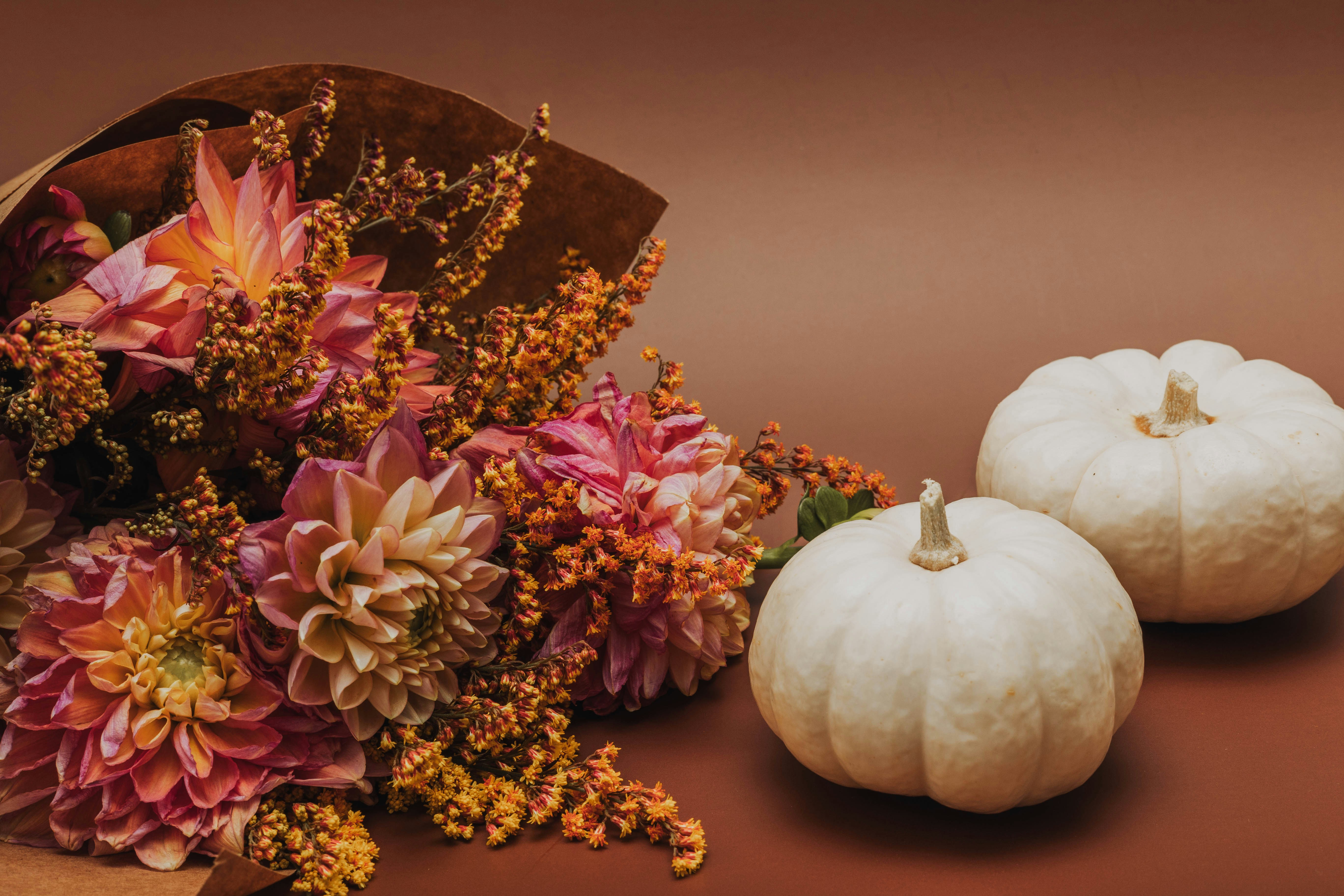 two white pumpkins sitting next to a bouquet of flowers