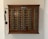 A vintage wooden telephone switchboard featuring multiple round dials with numbers and an antique telephone receiver attached to the side. The board has rows of metallic elements and numeric labels beneath each dial.