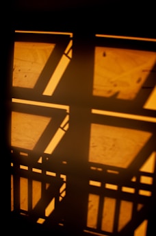 Geometric shadows and light patterns create an abstract design on a surface, with rectangular and linear shapes overlapping.