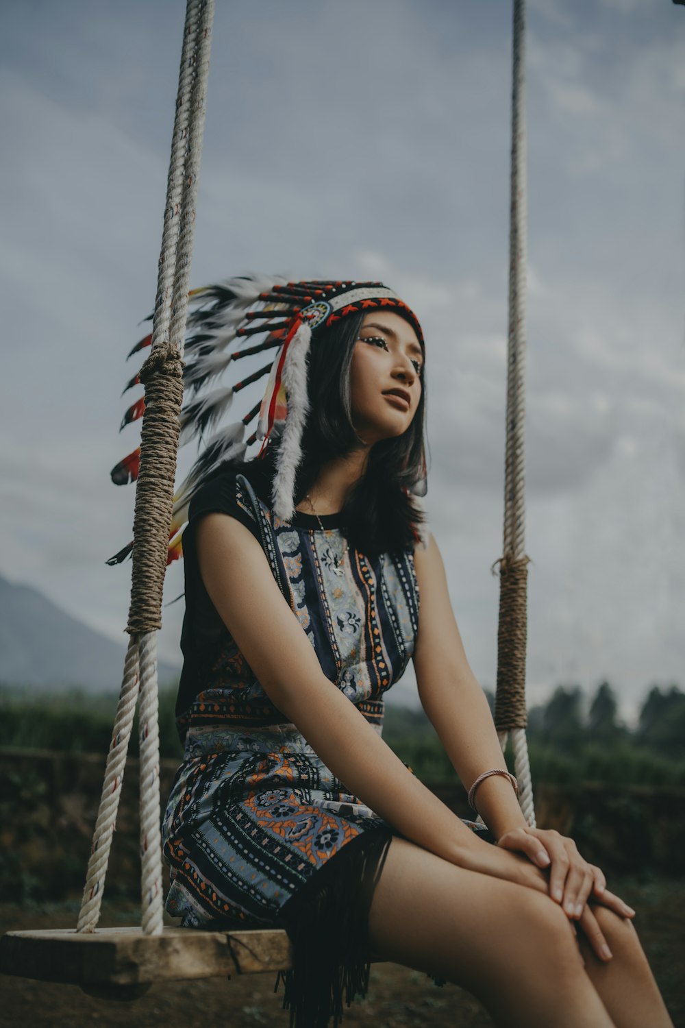 a woman sitting on a swing wearing a headdress