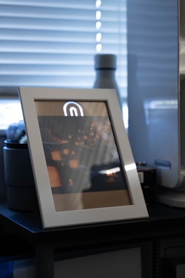 A modern photo frame with a stunning sunset photo inside, placed on a wooden table.