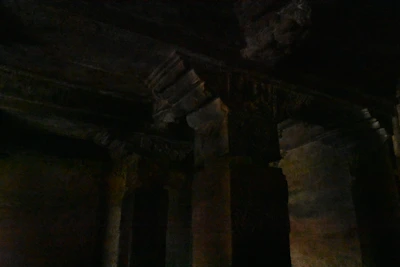 A dimly lit ancient temple interior with flickering candlelight casting shadows on worn stone carvings.