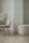 A modern, minimalist room featuring a cozy armchair with a fluffy cushion and a matching round ottoman. Both furniture pieces have a soft, textured fabric in a light cream color. They are set against a light-colored wall with a unique architectural design.