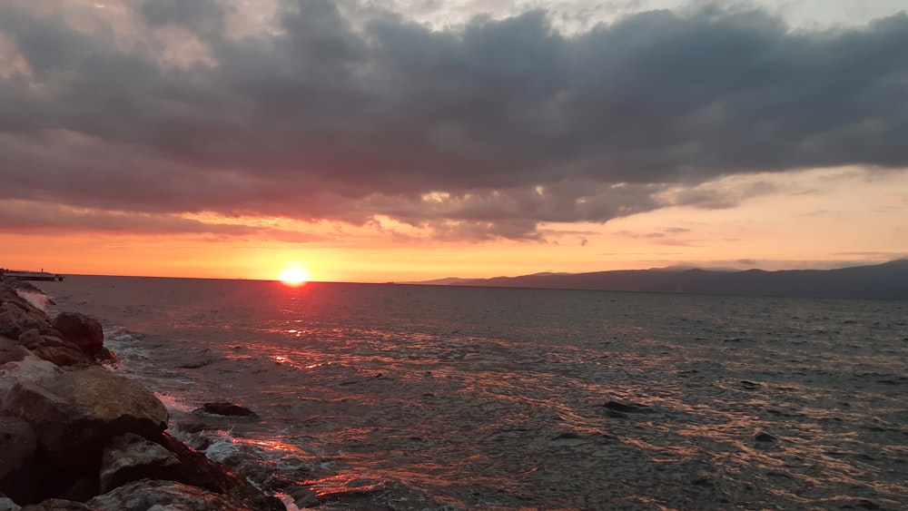 the sun is setting over the water and rocks