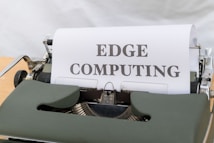 A vintage typewriter is displaying a sheet of paper with the words 'EDGE COMPUTING' typed in bold letters. The typewriter features a dark green body and metal components, set against a soft white background.
