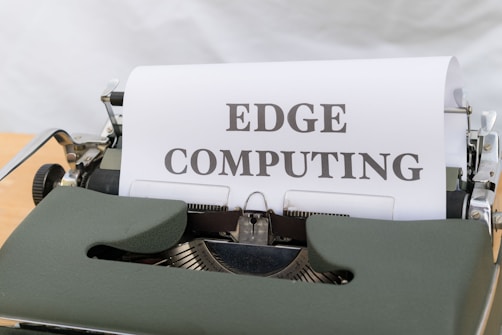 A vintage typewriter is displaying a sheet of paper with the words 'EDGE COMPUTING' typed in bold letters. The typewriter features a dark green body and metal components, set against a soft white background.