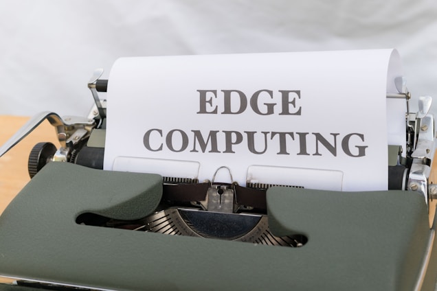 A vintage typewriter is displaying a sheet of paper with the words 'EDGE COMPUTING' typed in bold letters. The typewriter features a dark green body and metal components, set against a soft white background.