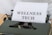 A vintage typewriter holds a sheet of paper with the words 'WELLNESS TECH' typed in large, bold letters. The typewriter is in a shade of olive green, with a focus on the metal and mechanical components. The paper is placed neatly in the roller, ready for typing more text.