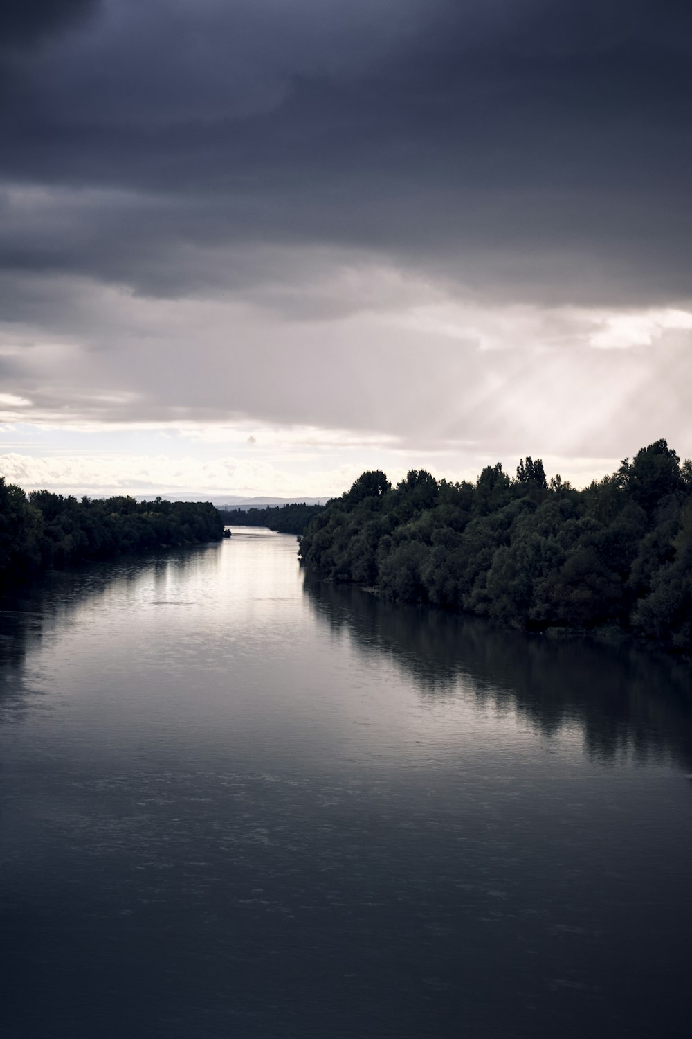 a body of water surrounded by trees under a cloudy sky