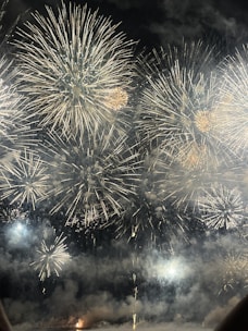 A spectacular display of large fireworks illuminating the night sky with bursts of bright, colorful lights and smoke. The fireworks create intricate patterns with golden and white hues, adding a sense of festivity and celebration.
