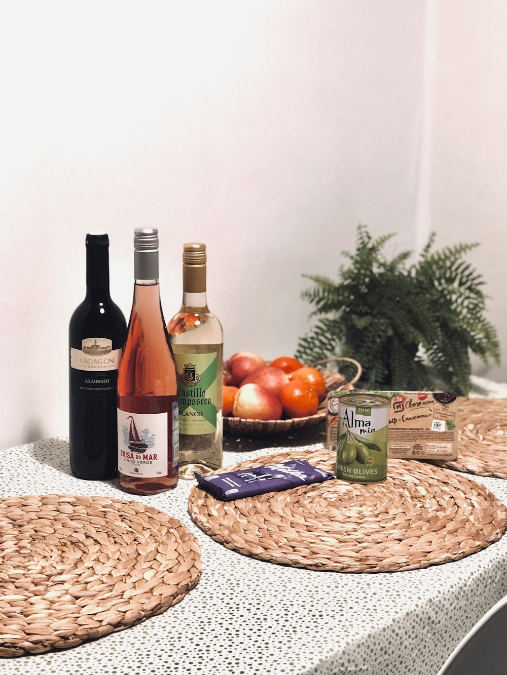 a table topped with a bowl of fruit and bottles of wine