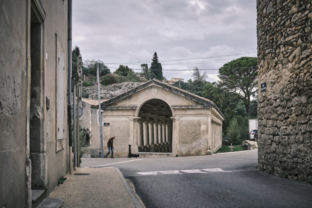 a man walking down a street next to a stone building