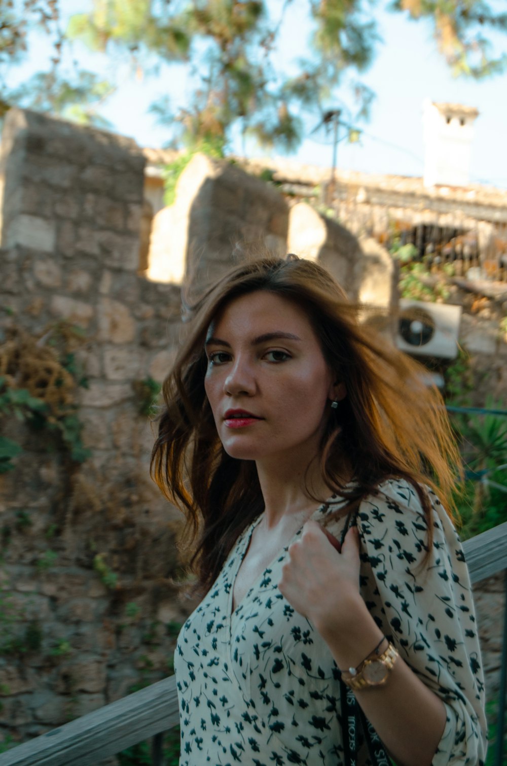 a woman walking down a street next to a stone wall