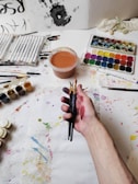 Close-up of hands crafting colorful art pieces surrounded by paint and brushes.