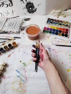 Close-up of hands crafting colorful art pieces surrounded by paint and brushes.