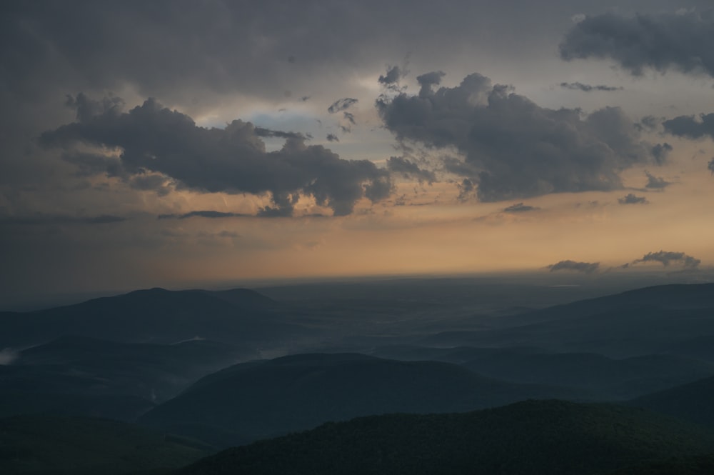 the sun is setting over the mountains with dark clouds