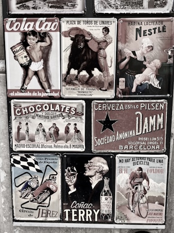 A collage of vintage advertisements with various themes, including a boy holding Cola Cao, a bullfighting poster, a Nestlé advertisement featuring a mother and child, and other ads for chocolate, beer, motorcycles, cognac, and cycling. The style is retro, and the images are arranged on a textured wall, each with distinct graphics and typography.