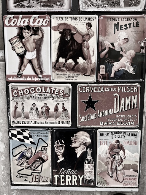 A collage of vintage advertisements with various themes, including a boy holding Cola Cao, a bullfighting poster, a Nestlé advertisement featuring a mother and child, and other ads for chocolate, beer, motorcycles, cognac, and cycling. The style is retro, and the images are arranged on a textured wall, each with distinct graphics and typography.