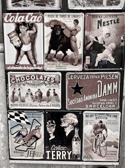 A collage of vintage advertisements with various themes, including a boy holding Cola Cao, a bullfighting poster, a Nestlé advertisement featuring a mother and child, and other ads for chocolate, beer, motorcycles, cognac, and cycling. The style is retro, and the images are arranged on a textured wall, each with distinct graphics and typography.