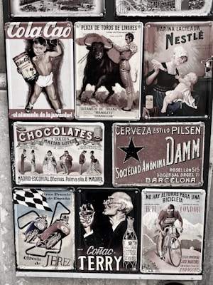 A collage of vintage advertisements with various themes, including a boy holding Cola Cao, a bullfighting poster, a Nestlé advertisement featuring a mother and child, and other ads for chocolate, beer, motorcycles, cognac, and cycling. The style is retro, and the images are arranged on a textured wall, each with distinct graphics and typography.