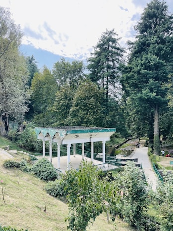 An airy pavilion in a green park setting with elegant arched elements and visitors strolling around.