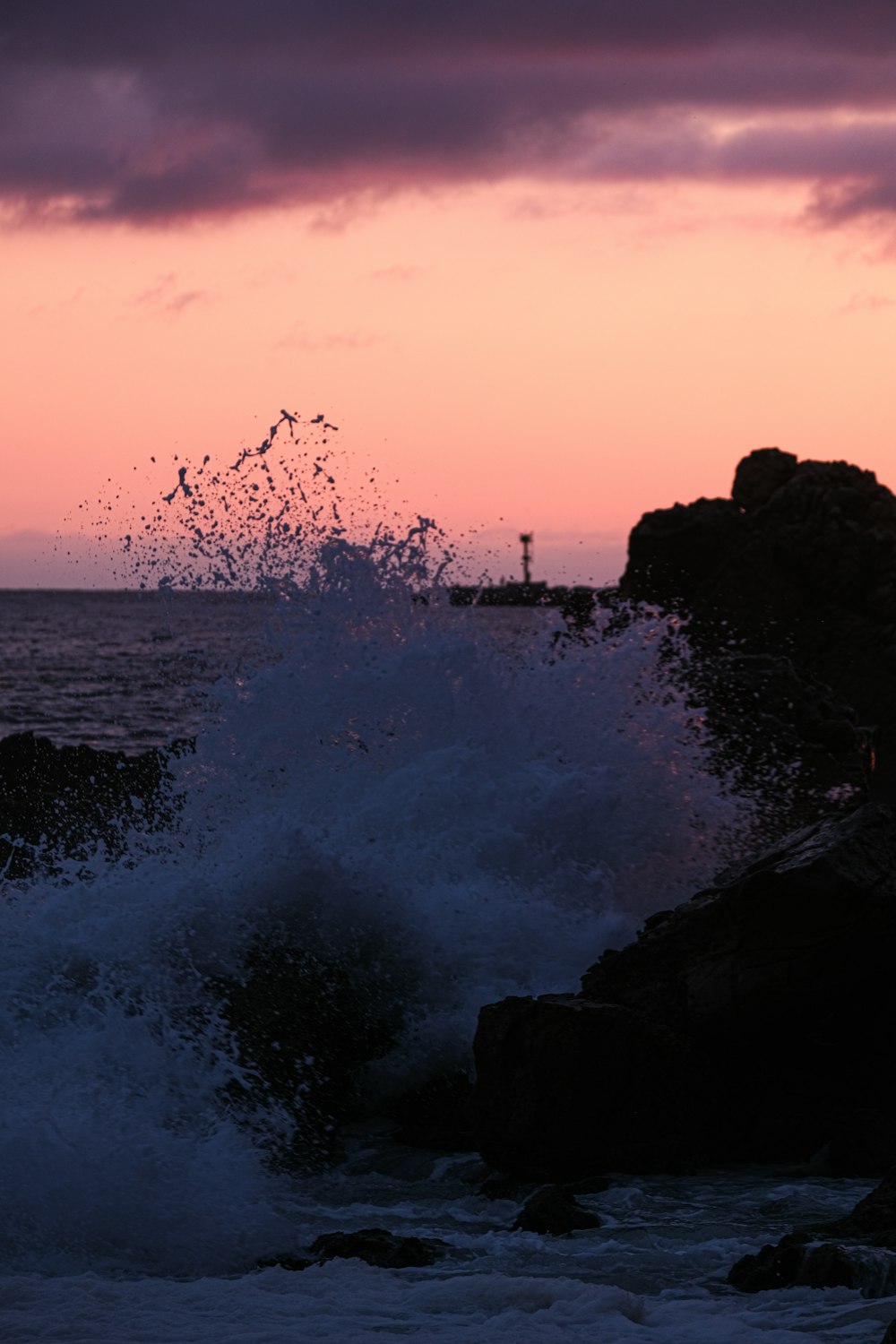 a wave crashing against a rocky shore at sunset