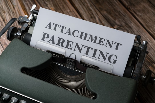 A vintage typewriter with a sheet of paper partially inserted, displaying the words 'ATTACHMENT PARENTING'. The typewriter is placed on a wooden surface, adding a rustic and nostalgic touch to the scene.
