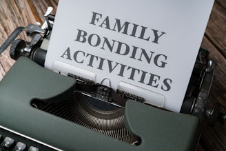 A vintage typewriter with a piece of paper inserted into it. The text 'FAMILY BONDING ACTIVITIES' is typed on the paper in large block letters. The typewriter is green and situated on a wooden surface.