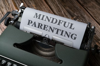 A close-up of a vintage typewriter with a sheet of paper inserted, displaying the text 'MINDFUL PARENTING' in bold letters. The typewriter is placed on a wooden surface.