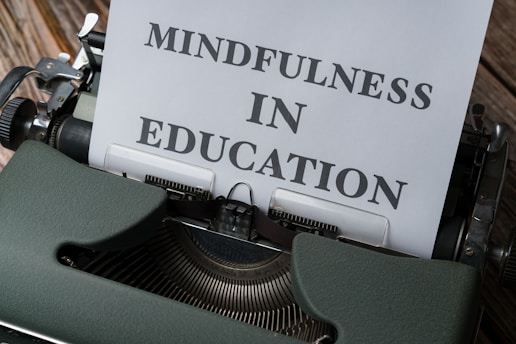 A vintage typewriter with a sheet of paper that has the words 'Mindfulness in Education' typed on it. The typewriter is an old-fashioned, dark green model with metal components, placed on a wooden surface.