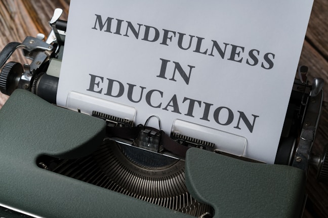 A vintage typewriter with a sheet of paper that has the words 'Mindfulness in Education' typed on it. The typewriter is an old-fashioned, dark green model with metal components, placed on a wooden surface.