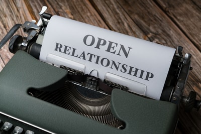 A vintage typewriter with a piece of paper that reads 'OPEN RELATIONSHIP' in bold letters. The typewriter is set on a wooden surface, giving an old-fashioned and rustic feel.
