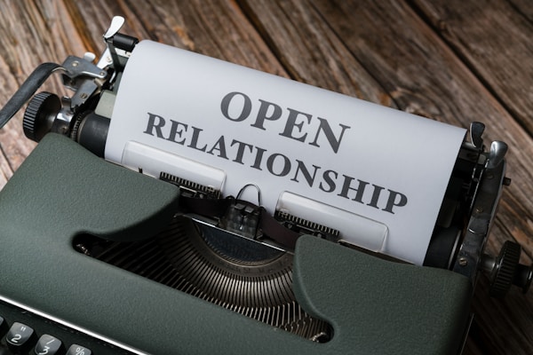 A vintage typewriter with a piece of paper that reads 'OPEN RELATIONSHIP' in bold letters. The typewriter is set on a wooden surface, giving an old-fashioned and rustic feel.