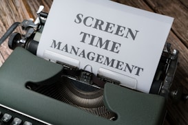 A vintage typewriter with a piece of paper inserted that reads 'Screen Time Management' in bold fonts. The machine sits on a wooden surface, suggesting an old or rustic setting.