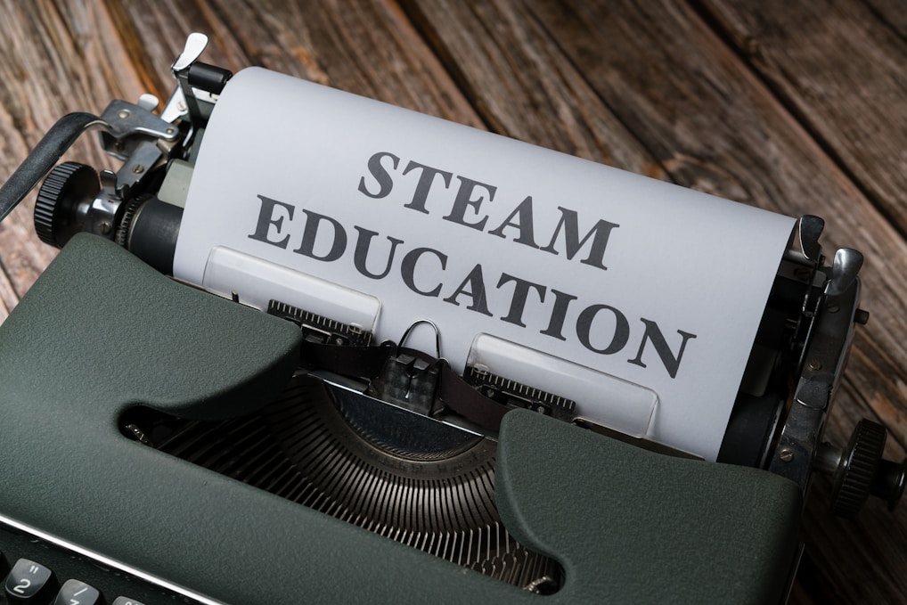 An old-fashioned typewriter with a sheet of paper inserted, displaying the words 'STEAM EDUCATION' in bold letters. The typewriter rests on a wooden surface, giving a vintage look.
