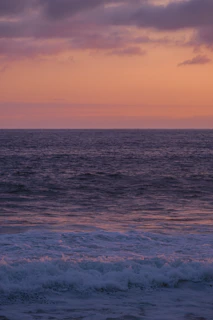 A serene ocean sunset with gentle waves reflecting warm hues of orange and pink.