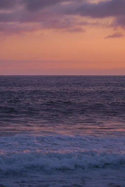 A serene ocean sunset with gentle waves reflecting warm hues of orange and pink.