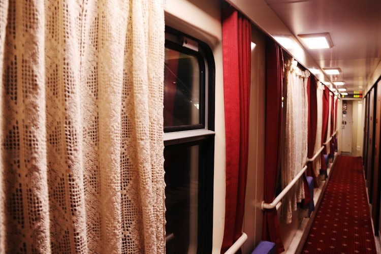 A train corridor at night lit by dim overhead lights with compartment doors along the side