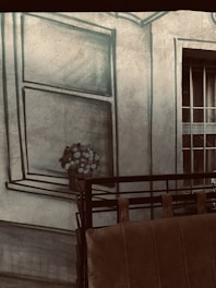 A textured wall features a painted window with a bouquet of flowers, creating a trompe-l'oeil effect. In front of the wall, there is a brown leather sofa with a metal railing.